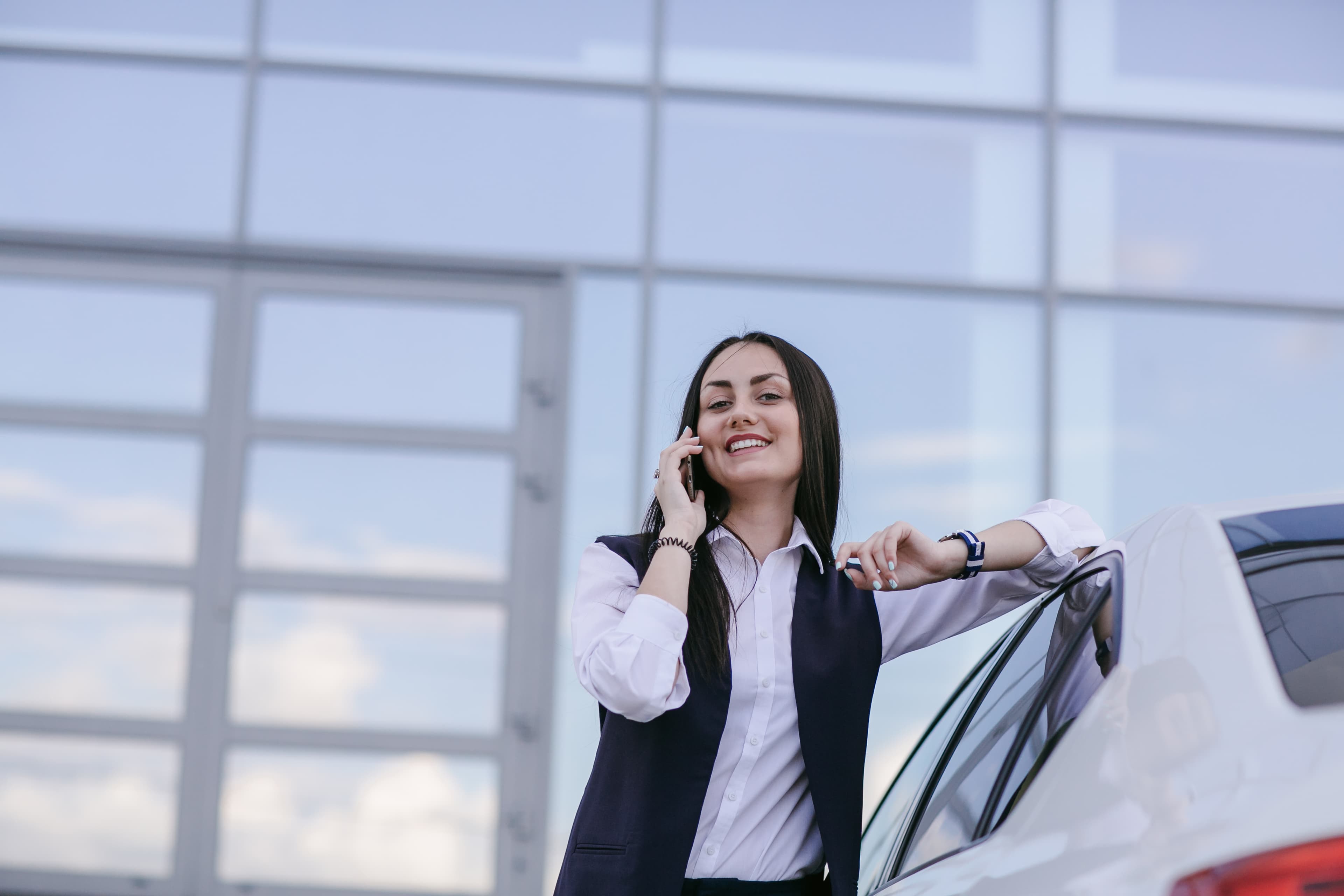 Mujer sonriente hablando por teléfono junto a su auto nuevo financiado con Derco